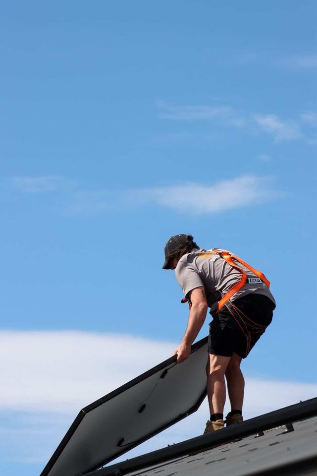 Installer lifting a solar panel into place on a roof against a blue sky
