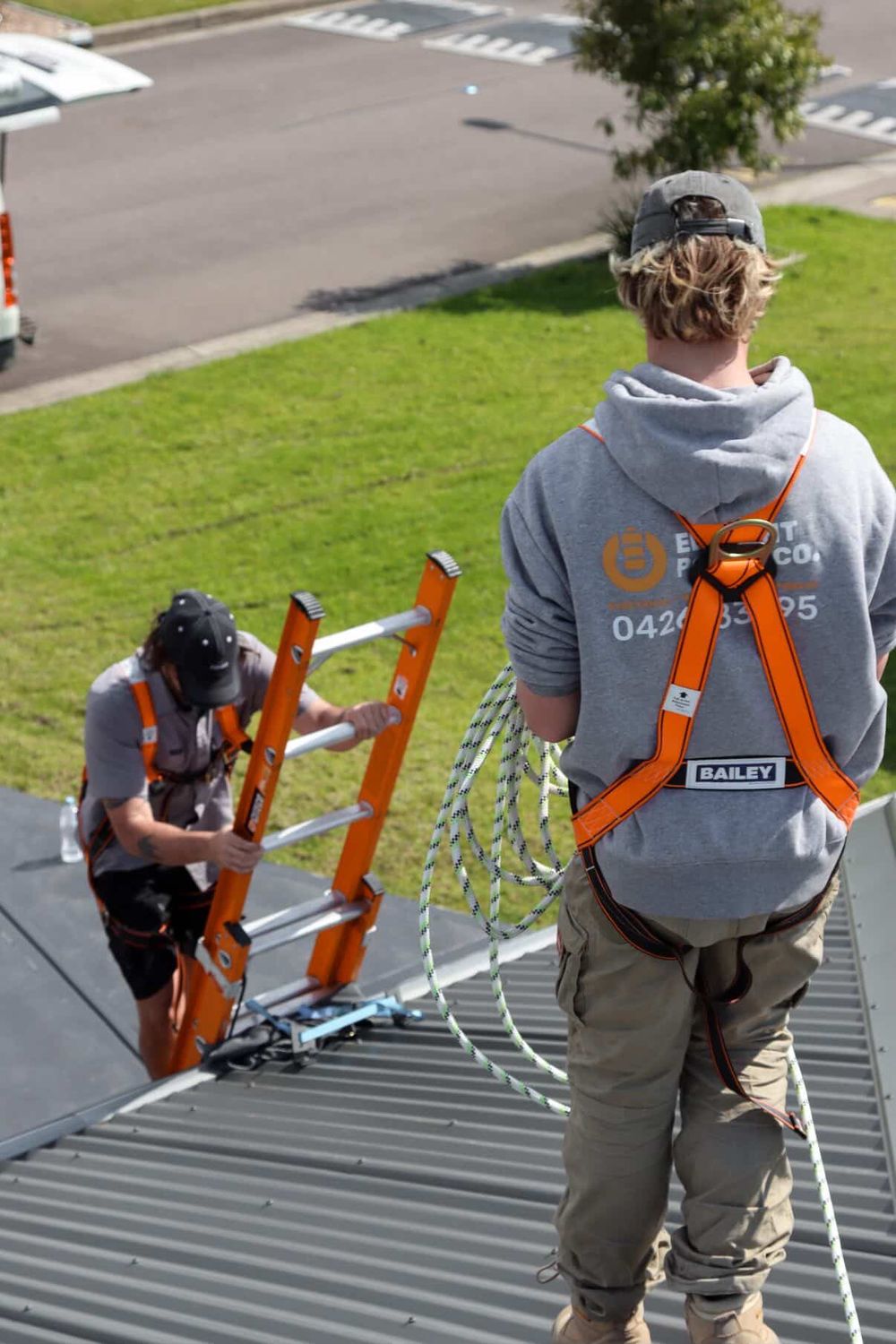 Two Element Power Co installers on a roof, one climbing the access ladder, one coiling a safety rope